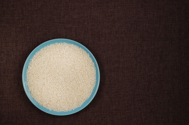 Vue de dessus, gros plan. Assiette bleue remplie de croup de riz blanc. Fond de lin foncé.