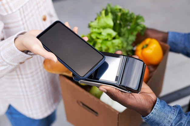 Vue de dessus en gros plan d'une femme payant la livraison d'épicerie via un smartphone NFC