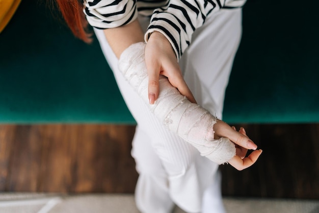 Vue de dessus en gros plan d'une jeune femme méconnaissable souffrant de douleur avec la main droite cassée enveloppée dans un bandage en plâtre massant doucement le bras blessé