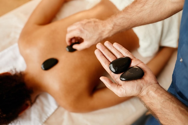 Vue de dessus gros plan d'un jeune homme posant des pierres sur le dos d'une jeune femme dans un espace de copie de séance de spa relaxant