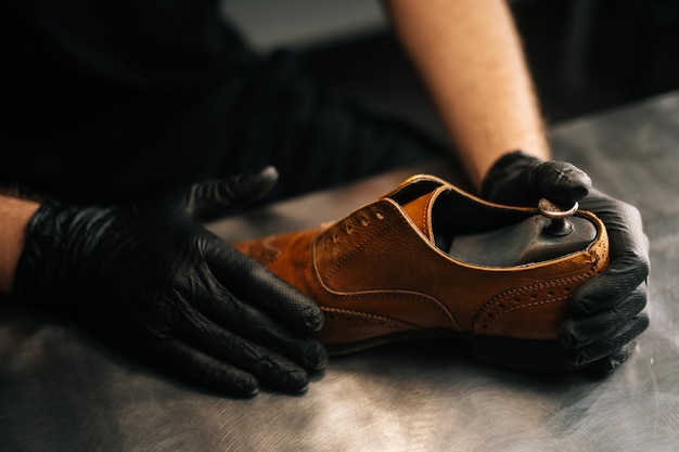 Vue de dessus en gros plan des mains du cordonnier cordonnier portant des gants noirs insère un patin en bois dans des chaussures en cuir marron clair usées