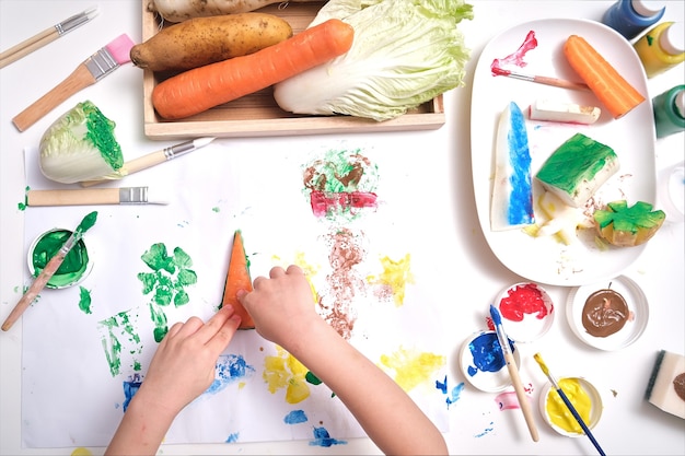 Vue de dessus gros plan des mains de tout-petit garçon enfant, enfant faisant des illustrations de l'estampage de légumes à la maison