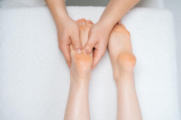 Vue de dessus en gros plan d'un masseur masculin massant les pieds à une jeune femme allongée sur une table de massage Physiothérapeute professionnel avec des mains fortes effectuant un massage des pieds Concept de soins de spa de massage
