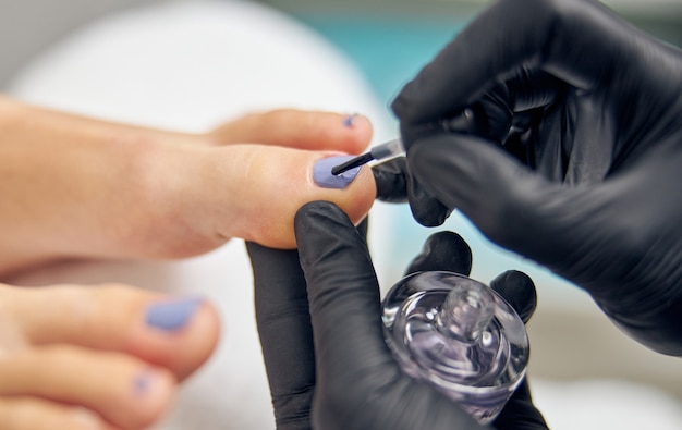 Vue de dessus en gros plan des pieds féminins pendant que l'artiste des ongles peint ses ongles d'orteil