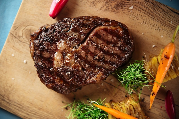 Vue de dessus gros plan sur steak de faux-filet de boeuf grillé avec pommes de terre sur la planche de bois