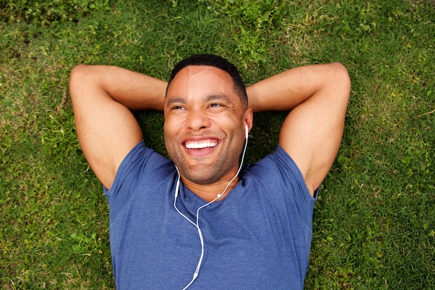 Photo vue de dessus heureux jeune homme africain couché sur l'herbe avec des écouteurs