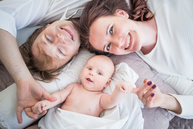 Vue De Dessus Heureux Positif Jeune Femme Mari De Famille Et Petit Bébé Nouveau-né Se Trouvent Sur Un Lit Douillet