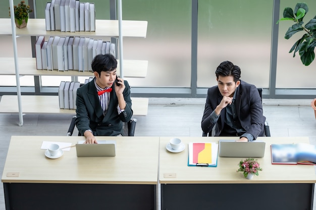 Vue de dessus Homme d'affaires asiatique homosexuel LGBT parlant avec un téléphone portable tout en travaillant sur un ordinateur portable et un groupe de gens d'affaires dans la salle de réunion d'un bureau moderne
