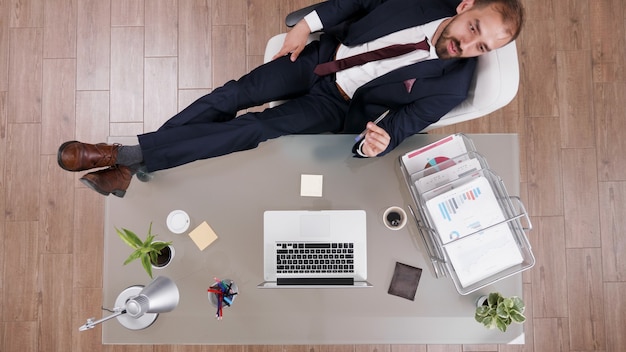 Vue de dessus d'un homme d'affaires prospère en costume debout les pieds sur le bureau en train de réfléchir aux idées d'investissements de l'entreprise. Directeur exécutif travaillant à la stratégie commerciale dans le bureau d'entreprise de démarrage