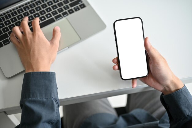 Vue de dessus d'un homme d'affaires travaillant à son bureau à l'aide d'un ordinateur portable et tenant un smartphone