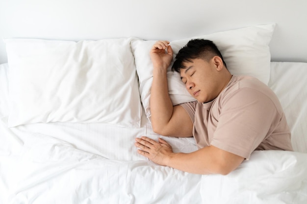 Vue de dessus d'un homme asiatique paisible dormant dans un lit confortable