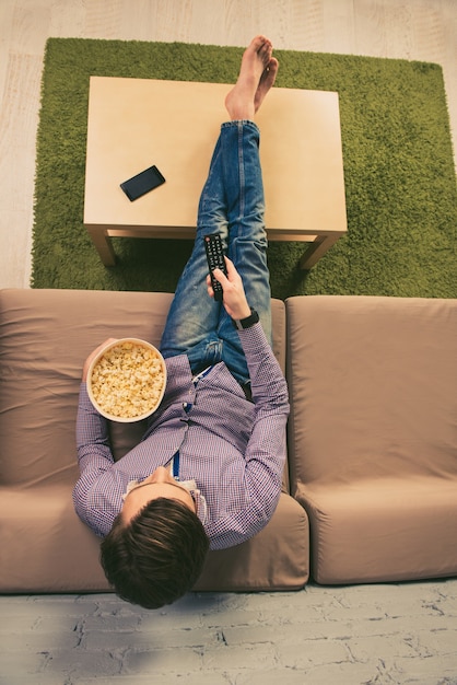 Vue de dessus de l'homme aux pieds nus devant la télé avec du pop-corn