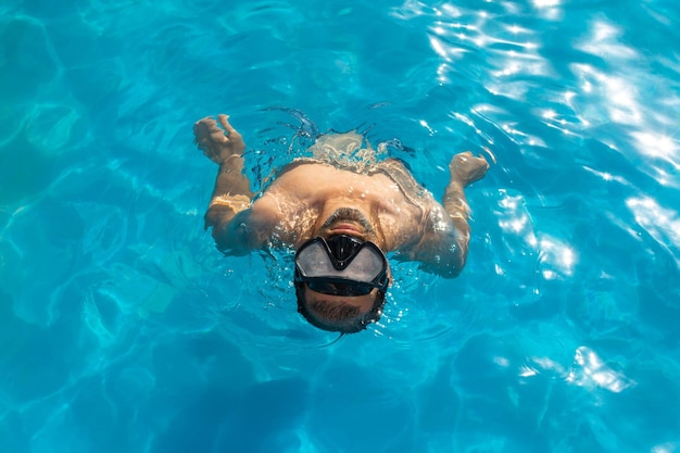 Vue de dessus d'un homme avec un masque de plongée à l'intérieur d'une piscine regardant directement la caméra