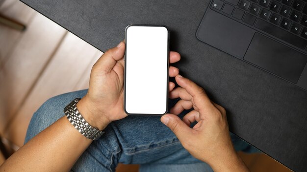 Vue de dessus d'un homme tenant un smartphone ou un téléphone portable avec ses deux mains Maquette d'écran vide de téléphone