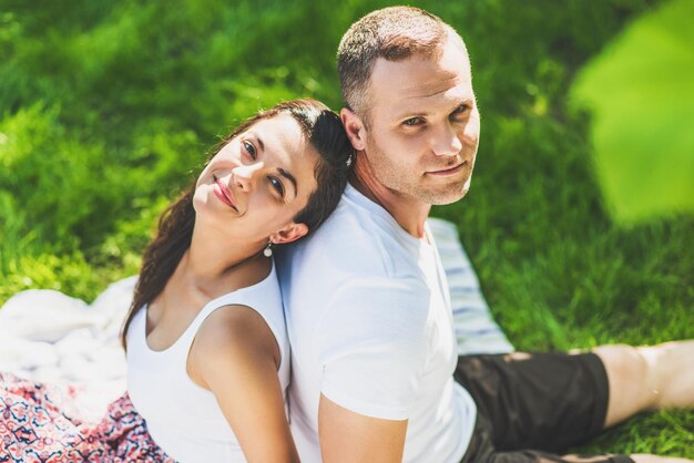 Vue de dessus horizontale d'un beau couple mignon amoureux assis sur une couverture de pique-nique Homme heureux caucasien et femme brune souriante regardant assis sur des rayures plaid sur l'herbe verte