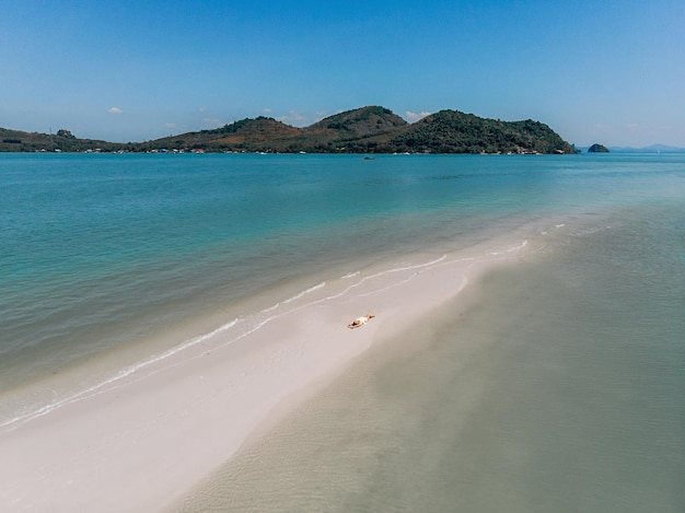 Vue de dessus d'une immense plage d'azur avec du sable blanc et chaud, sur laquelle un homme allongé et à côté de lui les ruisseaux de la mer. Beau concept de plage.
