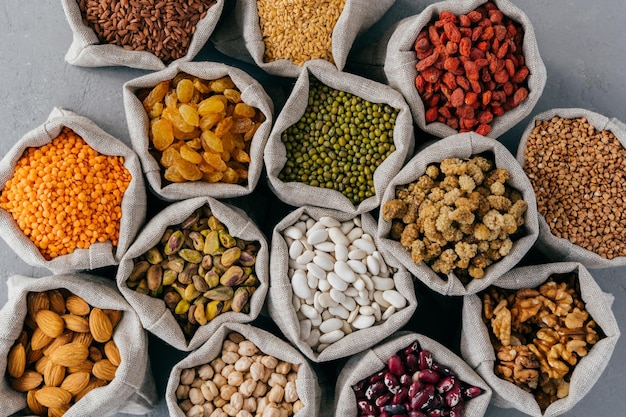 Vue de dessus des ingrédients secs sains dans des sacs en toile de jute Céréales nutritives et fruits secs garbanzo aux amandes pistache goji sarrasin mûre légumineuse dans des sacs en tissu