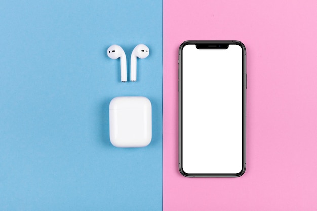 Vue de dessus de l'iphone et des Apple AirPods sur fond rose et bleu