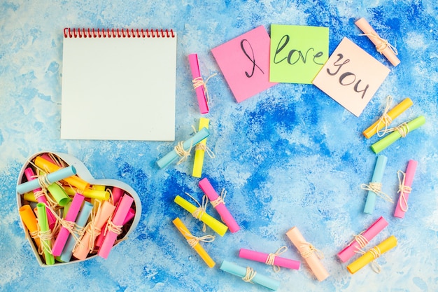 vue de dessus je t'aime écrit sur des notes autocollantes pour faire défiler les papiers de souhaits dans une boîte en forme de coeur sur fond bleu