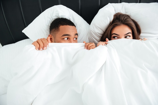 Vue de dessus d'un jeune couple amusant et ludique s'est couvert le visage avec une couverture au lit