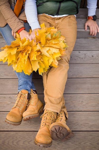 Vue de dessus sur un jeune couple tenant des bouquets de feuilles d'érable jaune et assis sur des escaliers en bois