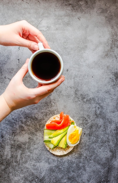 Vue de dessus de la jeune femme ayant une pause déjeuner. Galettes de riz croustillantes à l'avocat et au saumon frais salé. Mains masculines avec des aliments riches en graisses et en protéines et tasse de café. Espace pour le texte.