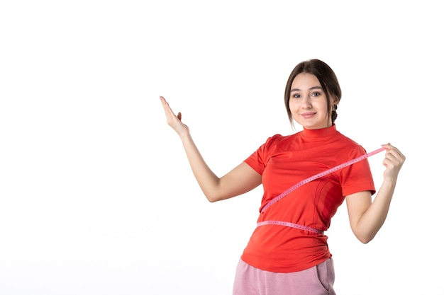 Vue de dessus d'une jeune femme confiante rassemblant ses cheveux vêtue d'un chemisier rouge-orange et tenant un mètre mesurant sa taille pointant vers le haut sur fond blanc