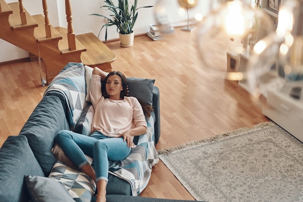 Vue de dessus d'une jeune femme détendue en vêtements décontractés reposant sur un canapé tout en passant du temps à la maison