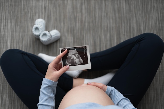 Vue de dessus d'une jeune femme enceinte assise sur le sol Maintient l'échographie du bébé près de l'abdomen