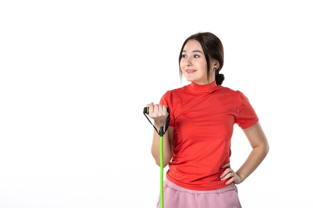 Vue de dessus d'une jeune femme heureuse rassemblant soigneusement ses cheveux vêtue d'un chemisier rouge orange et tenant un accessoire de sport de corde sur fond blanc