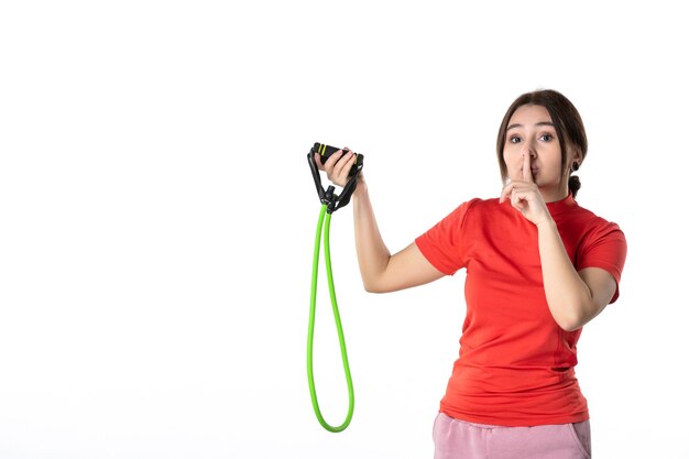 Vue de dessus d'une jeune femme rassemblant soigneusement ses cheveux vêtue d'un chemisier rouge orange et tenant un accessoire de sport de corde faisant un geste de silence sur fond blanc