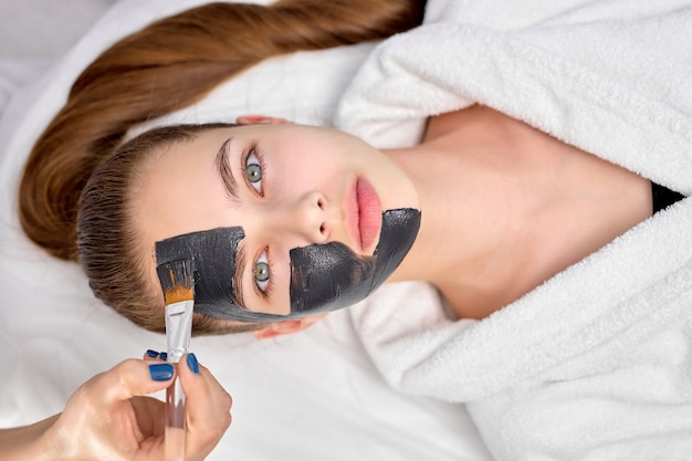 Vue de dessus sur une jeune femme séduisante dans un salon de spa avec masque noir sur le visage, espace pour copie