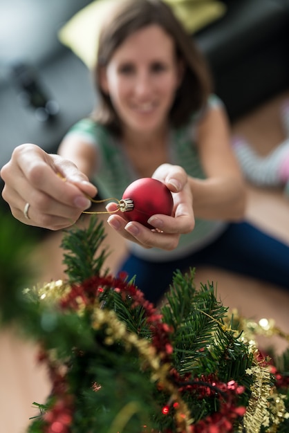 Vue de dessus d'une jeune femme souriante plaçant une boule de Noël rouge sur un arbre de Noël