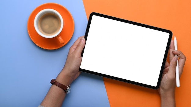 Vue de dessus d'une jeune femme tenant une tablette numérique avec un écran blanc sur fond bleu et orange à deux tons.