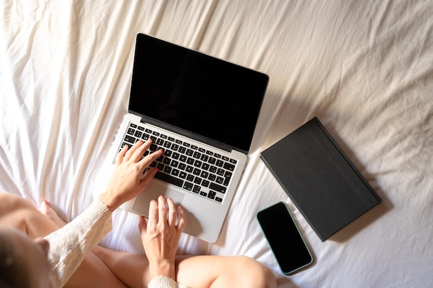 Vue de dessus d'une jeune femme utilisant un ordinateur portable au lit et se reposant à la maison. Fille relaxante dans sa chambre.