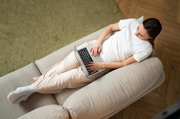 Vue de dessus d'une jeune femme utilisant sa tablette tout en se relaxant sur le canapé