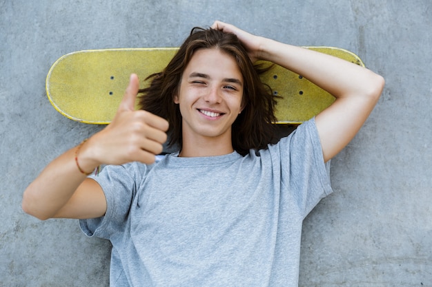 Vue de dessus d'un jeune garçon adolescent souriant, passer du temps au skate park, portant sur une planche à roulettes à une rampe, montrant les pouces vers le haut
