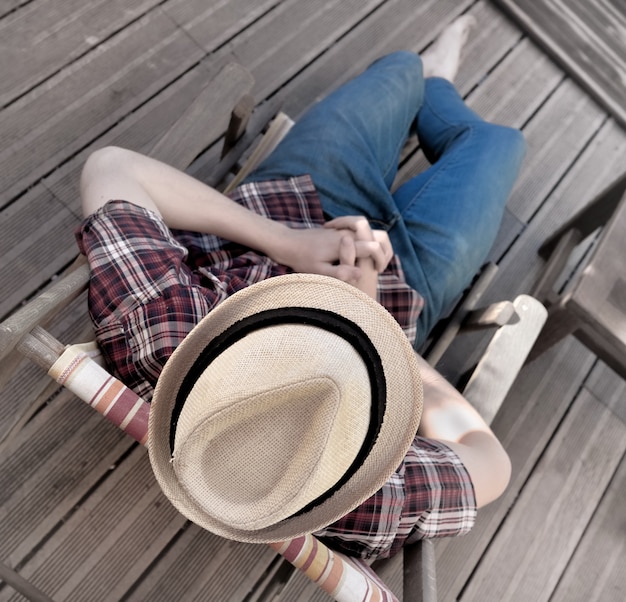 Photo vue de dessus sur un jeune homme avec un chapeau se détendre sur une chaise longue sur une terrasse en bois