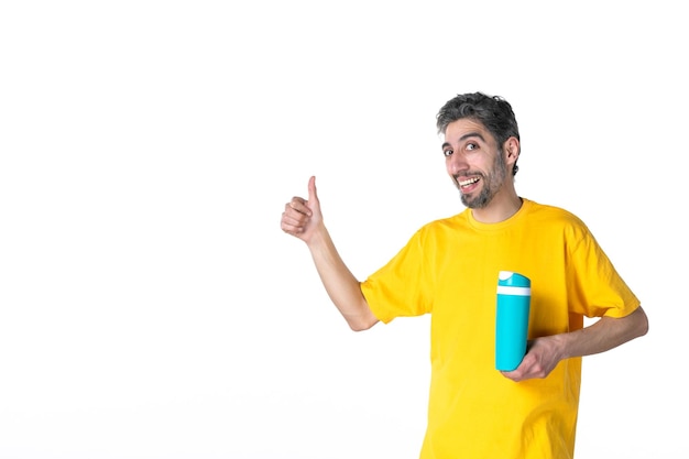 Vue de dessus d'un jeune homme souriant en chemise jaune et montrant un thermos bleu faisant un geste ok sur fond blanc