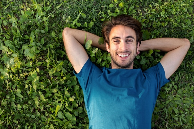 Vue de dessus d'un jeune homme souriant et heureux se relaxant allongé sur l'herbe en regardant la caméra Espace de copie