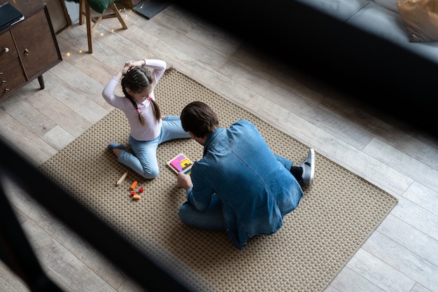 Vue de dessus d'un jeune père aimant allongé sur le sol avec sa fille s'amuser dans une activité amusante avec des briques de construction, passer du temps à la maison ensemble