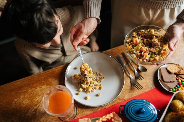 Vue de dessus d'un jeune père méconnaissable mettant de la salade sur une assiette à un fils enfant souriant préparant la table de Noël à la maison pour une fête de famille