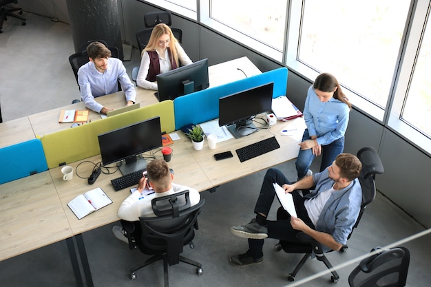 Vue de dessus de jeunes collègues modernes en tenue décontractée intelligente travaillant ensemble tout en passant du temps au bureau.