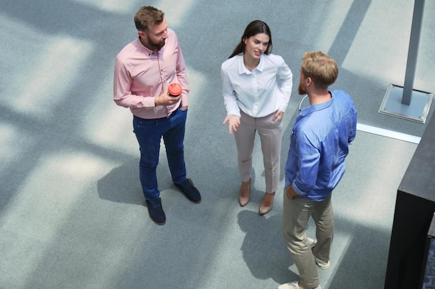 Vue de dessus de jeunes gens modernes dans des vêtements décontractés intelligents discutant des affaires tout en se tenant dans un bureau créatif