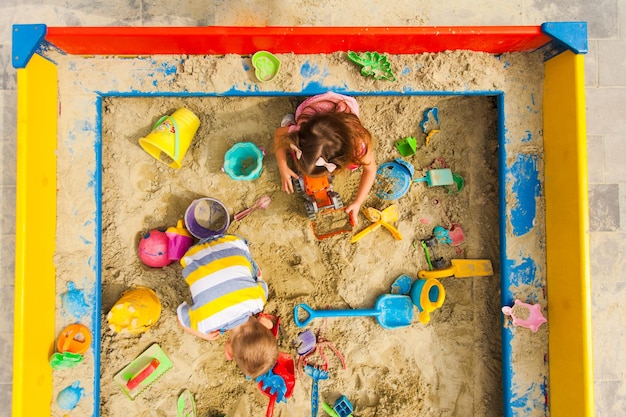 Vue de dessus des jeux pour enfants dans le bac à sable. Garçon et fille jouent à l'aire de jeux. Concept de créations, jouets colorés