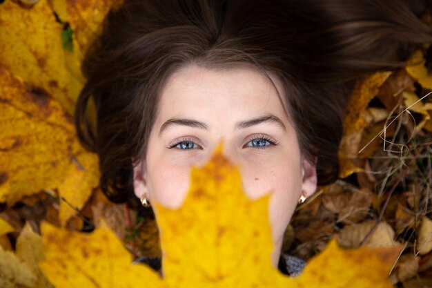 Vue de dessus d&#39;une jolie fille aux yeux bleus qui, à l&#39;automne, repose sur le sol et tient devant elle une belle feuille d&#39;érable jaune.