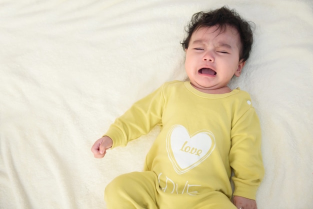 Vue De Dessus D'une Jolie Petite Asiatique Portant Une Robe Jaune, Allongée Sur Le Lit, Pleurant