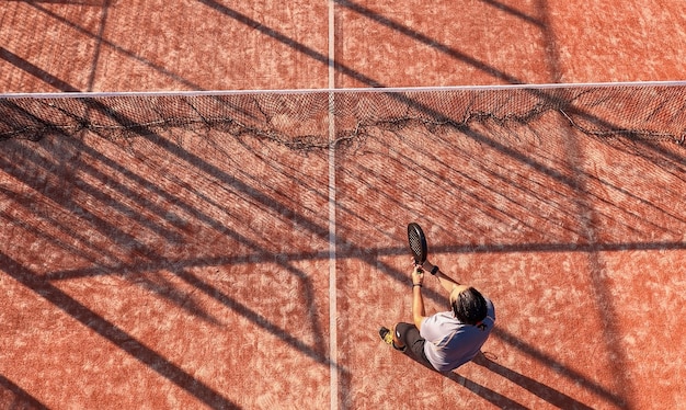 Vue de dessus d'un joueur de paddle-tennis debout près du filet avec la raquette sur un terrain extérieur.