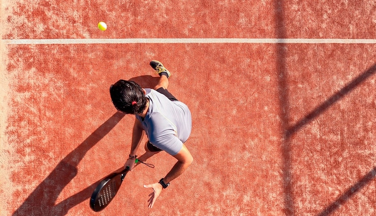 Photo vue de dessus d'un joueur de paddle-tennis qui frappe la balle avec la raquette sur un terrain extérieur. il est positionné près de la ligne.