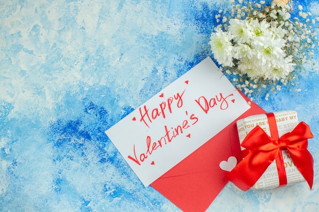vue de dessus joyeuse saint valentin écrite sur la lettre fleurs cadeau enveloppe rouge sur fond bleu espace libre